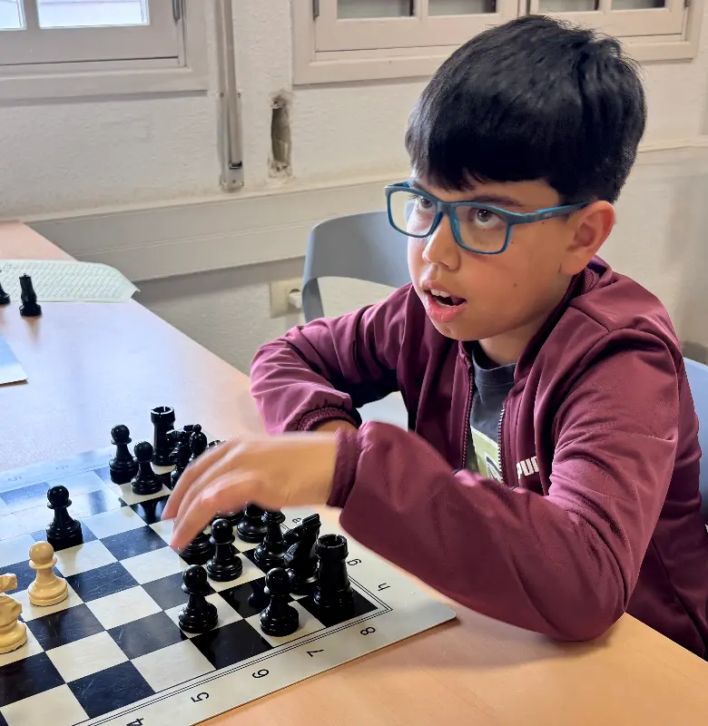 Boy with blue glasses reaches to move a chess piece on a checkered board during a game.