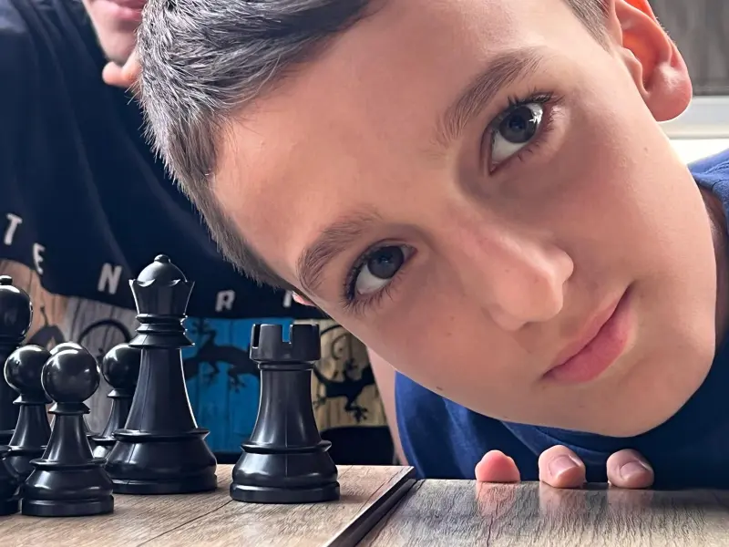 Boy leaning toward a chessboard, focused on the black pieces in the foreground.