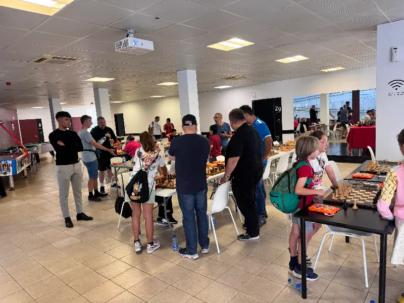 Group of players seated at tables in a bright hall, competing in a casual chess tournament.